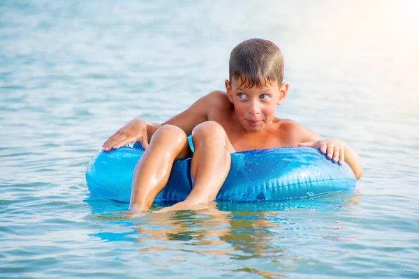 Chico con ojos astutos sentado en anillo inflable y divertirse en el mar — Foto de Stock