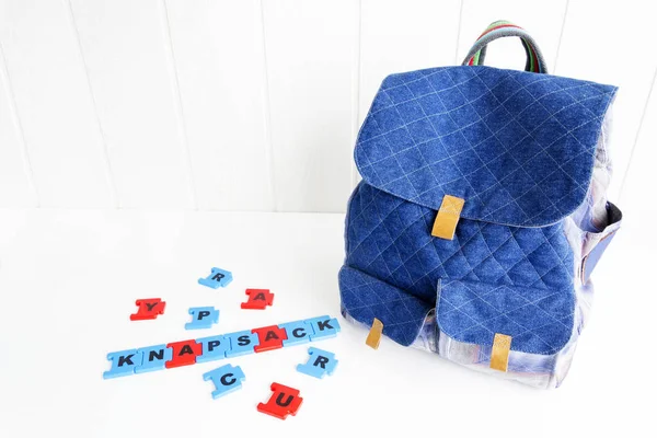 Blaue Tasche mit Puzzlebuchstaben auf weißem Tisch. Handgefertigter Rucksack für Reisende. — Stockfoto