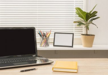 Dizüstü bilgisayar, sarı Not kitap, kalem, fotoğraf çerçevesi houseplant ve renk kalem karşı pencere ile modern çalışma alanı