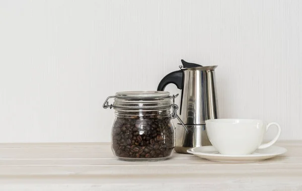 Set for coffee making: cup of coffee, coffee beans, percolator on white wooden table