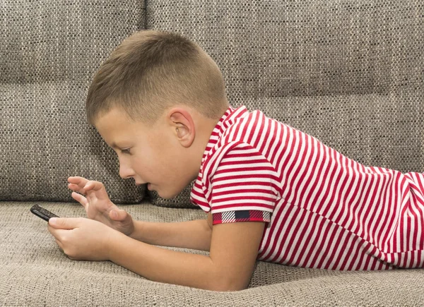Pre-tonåring leker med smartphone lade på soffa — Stockfoto