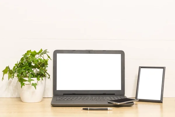 Laptop mock up on wooden table with photo frame, ivy plant in pot, pen, smartphone. Working space in loft. Interior photo