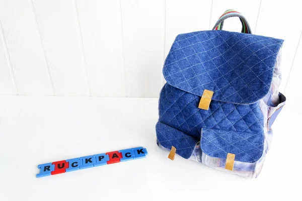 Blue bag with puzzle letters on white table. Hand made backpack for travelers. — Stock Photo, Image