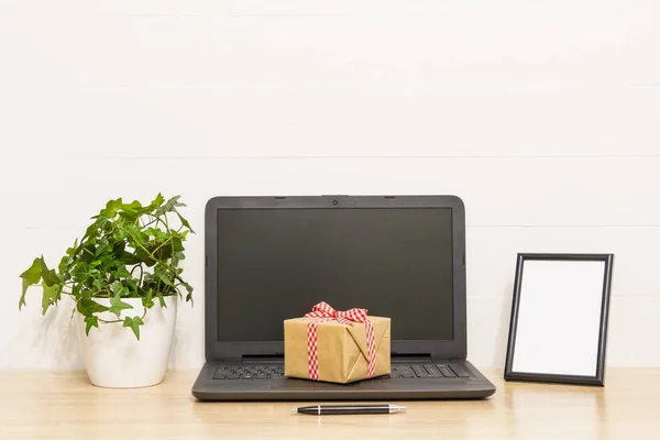 Portátil en mesa de madera con caja de regalo, planta de hiedra en maceta, marco de fotos, pluma. Espacio de trabajo en loft. Interior foto — Foto de Stock