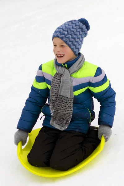 Kid slides down a hill on plate for driving on snow — Stock Photo, Image