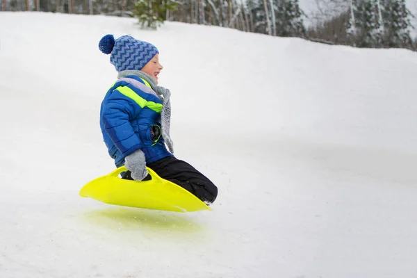 Παιδί πετά κάτω από έναν λόφο στο πιάτο για την οδήγηση στο χιόνι — Φωτογραφία Αρχείου