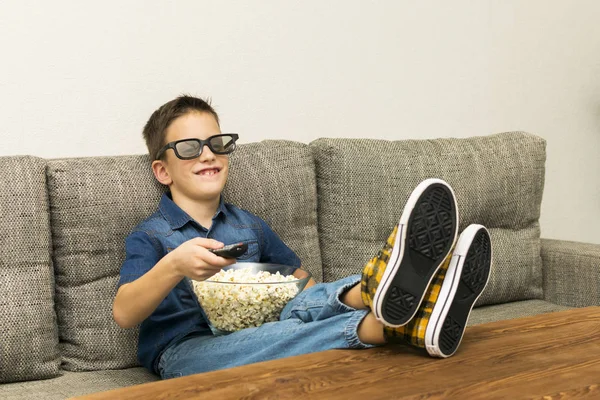 Divertido chico emocionado en gafas de cine viendo la televisión con palomitas de maíz y control de remo en la sala de estar — Foto de Stock