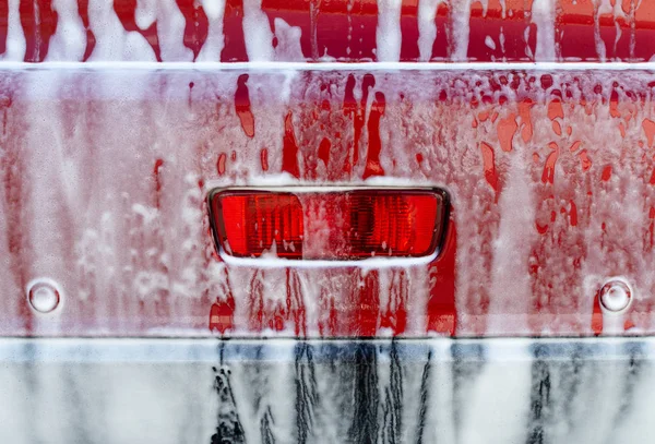 Πίσω όψη του κόκκινου αυτοκινήτου πλύσιμο με σαπούνι. Αυτοκίνητο καλυμμένο με λευκό αφρό. Επαγγελματική έννοια υπηρεσιών φροντίδας αυτοκινήτου. — Φωτογραφία Αρχείου