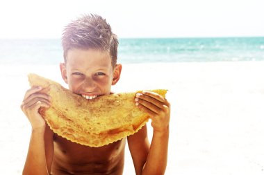 Street food concept. Young handsome hipster guy holding, eating meat pasty on the beach. Caucasian, Cheburek.
