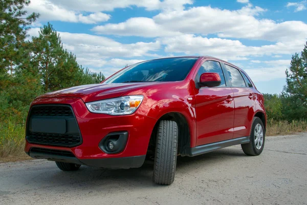 Hermoso coche rojo en la carretera en el bosque en el fondo . — Foto de Stock