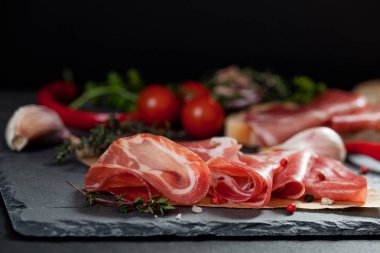 Jambon, domates, kırmızı biber ve otlar siyah taş üzerinde kurulu kayrak. 