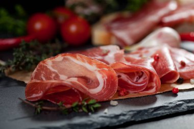 Jambon, domates, kırmızı biber ve otlar siyah taş üzerinde kurulu kayrak. 