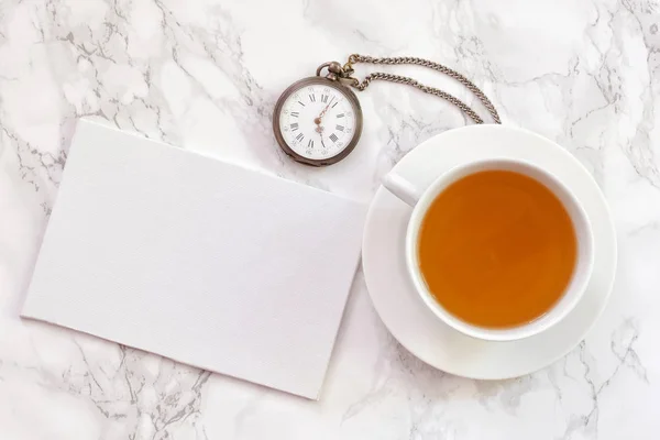 Tea time. Flat lay over light background with cup of tea, card and vintage pocket watch. Copy space for the text