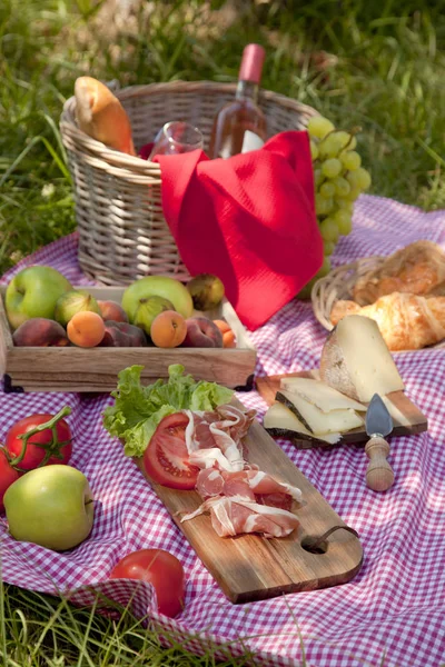 Picnic at the park on the grass: tablecloth, basket, healthy food, rose wine and accessories