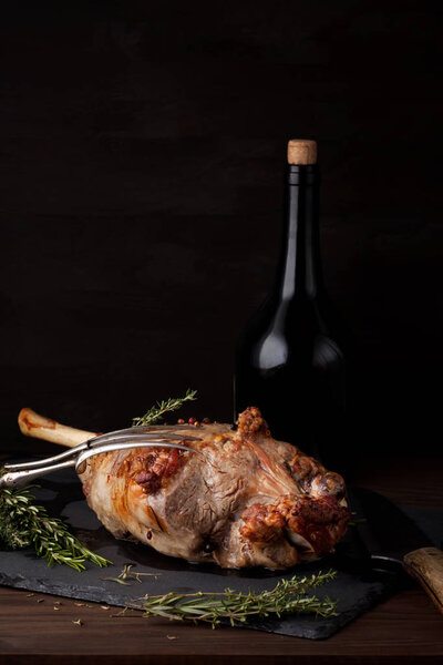 Freshly roasted lamb leg with herbs and bottle of red wine