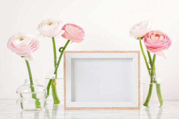 Poster frame mockup, front view, with decor elements, flowers and blank copy space over the white wall.