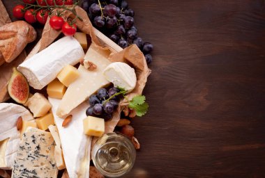 Variety of different cheese with wine, fruits and nuts. Camembert, goat cheese, roquefort, gorgonzolla, gauda, parmesan, emmental. Top view clipart