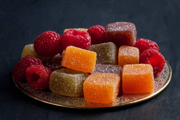 Close-up of colorful sweet fruit jelly candies or marmelade with raspberies on decorated metal plate. Concept of sweetness and healthy sweets made of fruits, berries and natural ingredients