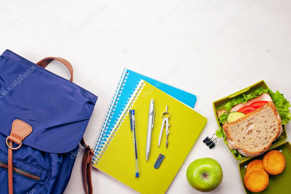 Student backpack, school supplies and fresh sandwich and apple for healthy lunch in the plastic lunch box