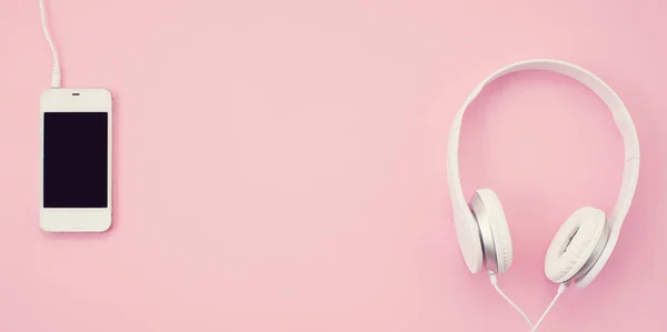 Top view of white earphones with smartphone on pink background. Online music concept