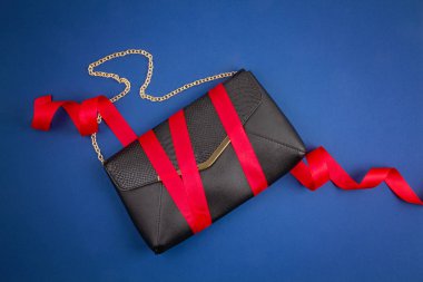 Koyu mavi arka planda kırmızı kurdeleli siyah el çantası.. 