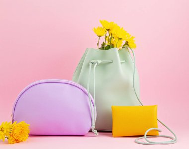 Parlak pastel renkte kızlar deri aksesuarlar: el kötü, çanta, makyaj çantası ve pembe arka planda çiçekler. 