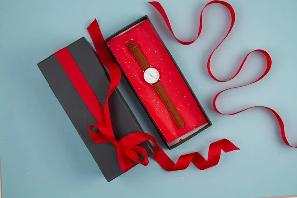 Reloj de mano de mujer empaquetado en la caja de regalo negro con cinta roja sobre el fondo azul — Foto de Stock