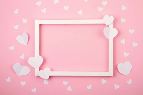 Papieren hartjes en wit frame over de roze pastelachtergrond. Liefde, Sint Valentijn, Moederdag, verjaardagskaarten, uitnodiging, feestelijk concept — Stockfoto