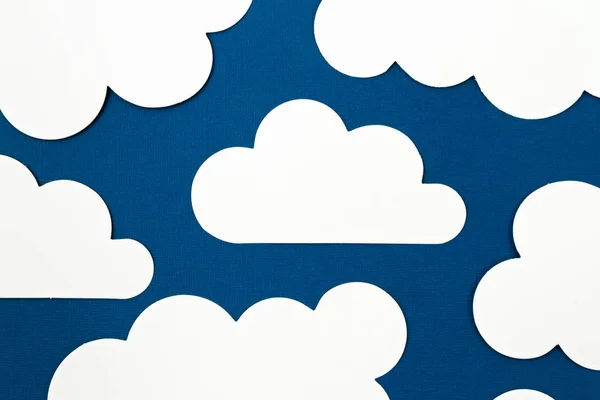 White paper cut out clouds over blue background.