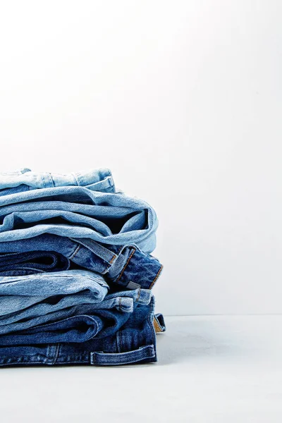 Pilha de jeans azuis clássicos sobre o fundo claro. Roupa urbana, guarda-roupa essencial básico, ideia de compras — Fotografia de Stock