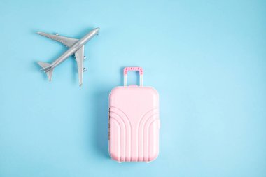 Mavi arka planda minyatür uçak ve bavul. Seyahat hazırlığı, turizm, havayolları, düşük maliyetli uçuşlar, bagaj paketleme konsepti. Üst manzara, düz uzanma.
