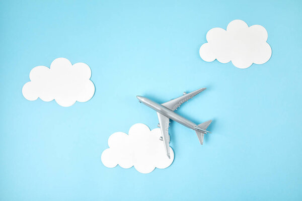Miniature airplane over blue background with paper clouds. Travel tourism, airlines, low cost flights concept. Top view, flat lay.