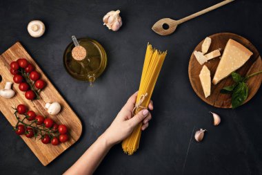 İtalyan makarnası pişirmek için spagetti ve malzeme tutan bir kadın. Spagetti, domates, yağ, sarımsak, parmezan. Geleneksel italyan kümes konseptinin en üst görüntüsü