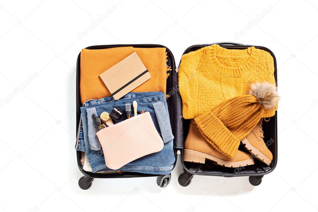 Flat lay with open suitcase with casual clothes for autumn, winter vacations over white background. Winter holidays, travel, tourism, flight luggage concept. Top view