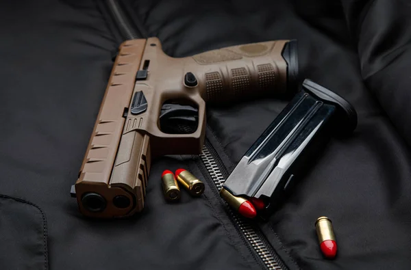 Een modern bruin pistool en munitie erop zitten op een donkere jas.. — Stockfoto