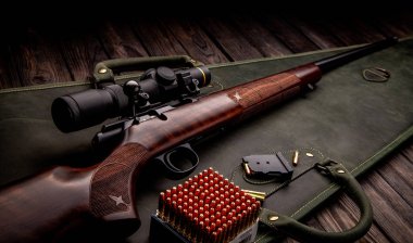 Klasik cıvata karabinası. 22 lr. Koyu ahşap arka planda teleskopik görüş açısı olan tahta bir poposu var. Silahın yanında bir tüfek için fişekler. Avcı takımı.
