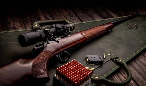 Classic bolt carbine .22lr with a wooden butt with a telescopic sight on a dark wooden background. Cartridges for a rifle next to a weapon. Hunter set. — Stock Photo, Image