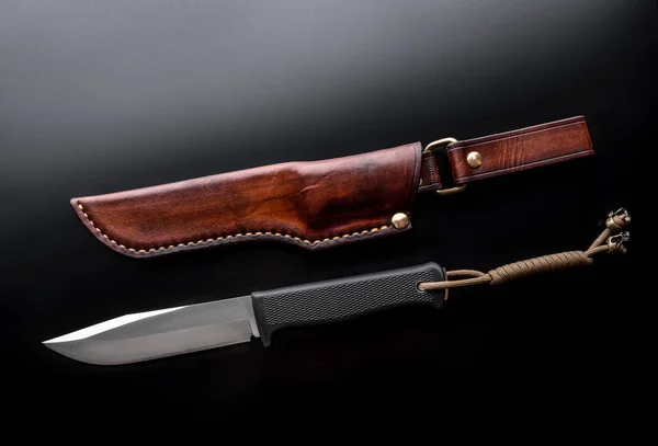 Un coltello da caccia moderno e una custodia in pelle per lui su un dorso scuro — Foto Stock