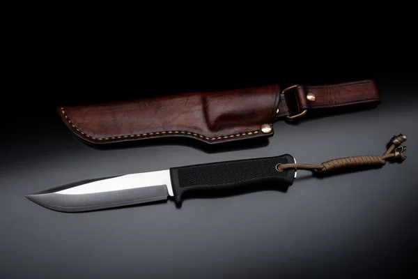 Un couteau de chasse moderne et un étui en cuir pour lui sur un dos sombre — Photo