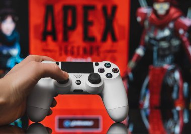 Odessa, Ukraine - February 9, 2020. White playstation 4 gamepad on the background of the game APEX Legends from EA Games. Apex Legends free to play Battle Royale shooting game.