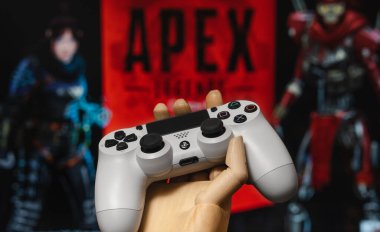 Odessa, Ukraine - February 9, 2020. White playstation 4 gamepad on the background of the game APEX Legends from EA Games. Apex Legends free to play Battle Royale shooting game.
