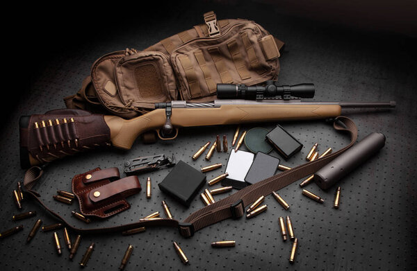 Modern bolted carbine and cartridges for it on a dark wooden table. Rifle with a telescopic sight on a dark background. Weapons for hunting, sports and self-defense. Postcard concept.