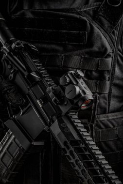 Bir adam koyu arkaplanda otomatik bir karabina tutuyor. Koyu renk bir arka plan. Elinde silah olan siyah giysili ve taktik yelekli bir savaşçı. Polis, güvenlik veya askeri afiş konsepti.