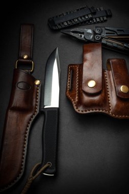 Karanlık bir arka planda av bıçağı ve çoklu alet. Bıçak ve çoklu aletin yanında kahverengi deri çantalar. Erkekler için kartpostal kavramı.