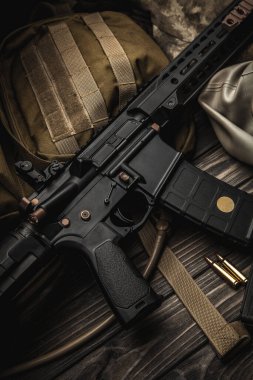 Ahşap bir masada modern otomatik karabina, sırt çantası ve gaz maskesi. Her türlü savaş koşuluna hazır bir avcı takımı..