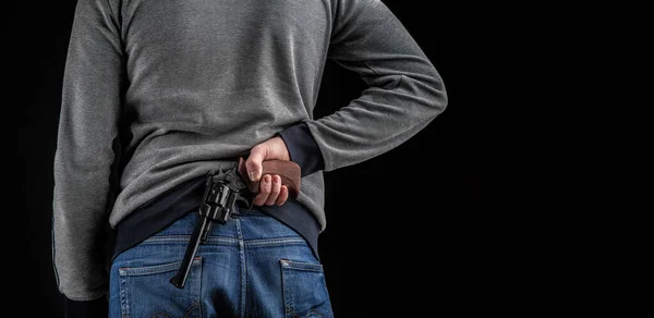 一个背着枪的男人的近身镜头一个穿牛仔裤 穿着灰色运动衫 深色背景下拿着武器的男人 — 图库照片