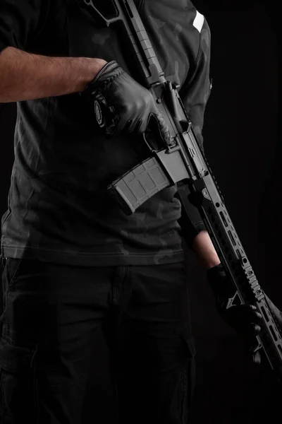 一个人在黑暗的背景上拿着自动卡宾枪 一个黑衣战士手里拿着武器警察 安全或军事人员的海报概念 — 图库照片