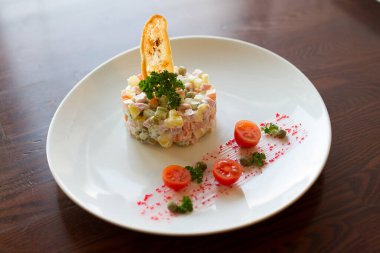 Beyaz tabakta, tahta masada Rus usulü salata.