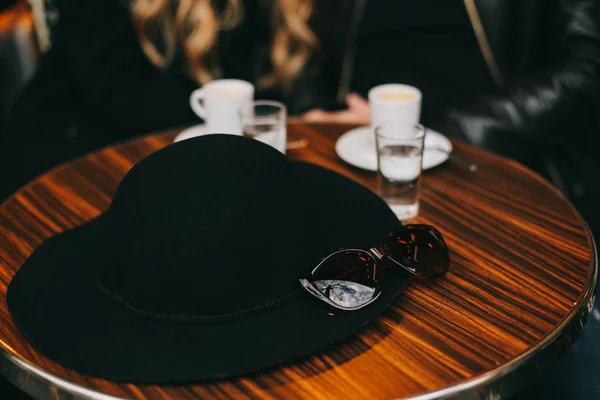 Black hat is laying on the table with two cups of coffee