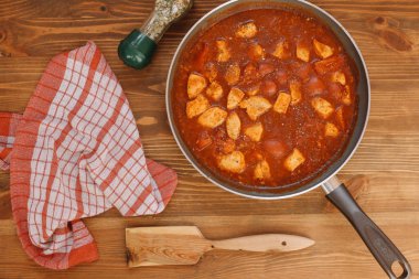 Domates ve baharat ahşap kürek, havlu, domates ve baharat şişe ile kahverengi ahşap zemin üzerinde bir tavada kızarmış tavuk parçaları